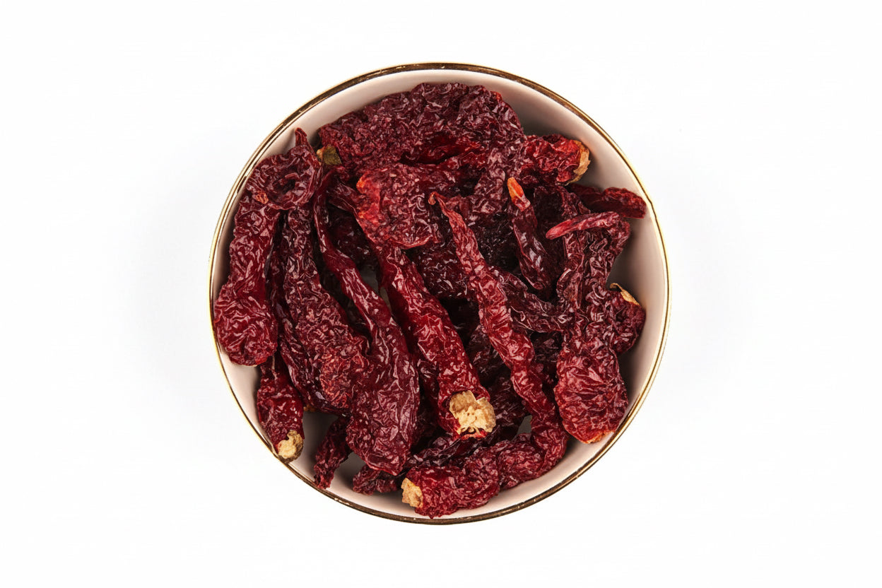 Dried red chili peppers in a white bowl with a gold rim on a white background